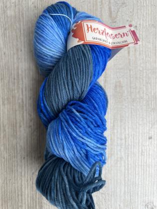 Handgefärbter Strang in Hellblau, Türkis und Mittelblau mit kleinen Farbsprenkelchen. Der Strang liegt auf hellem Holz, mit Herzfasern-Banderole.“